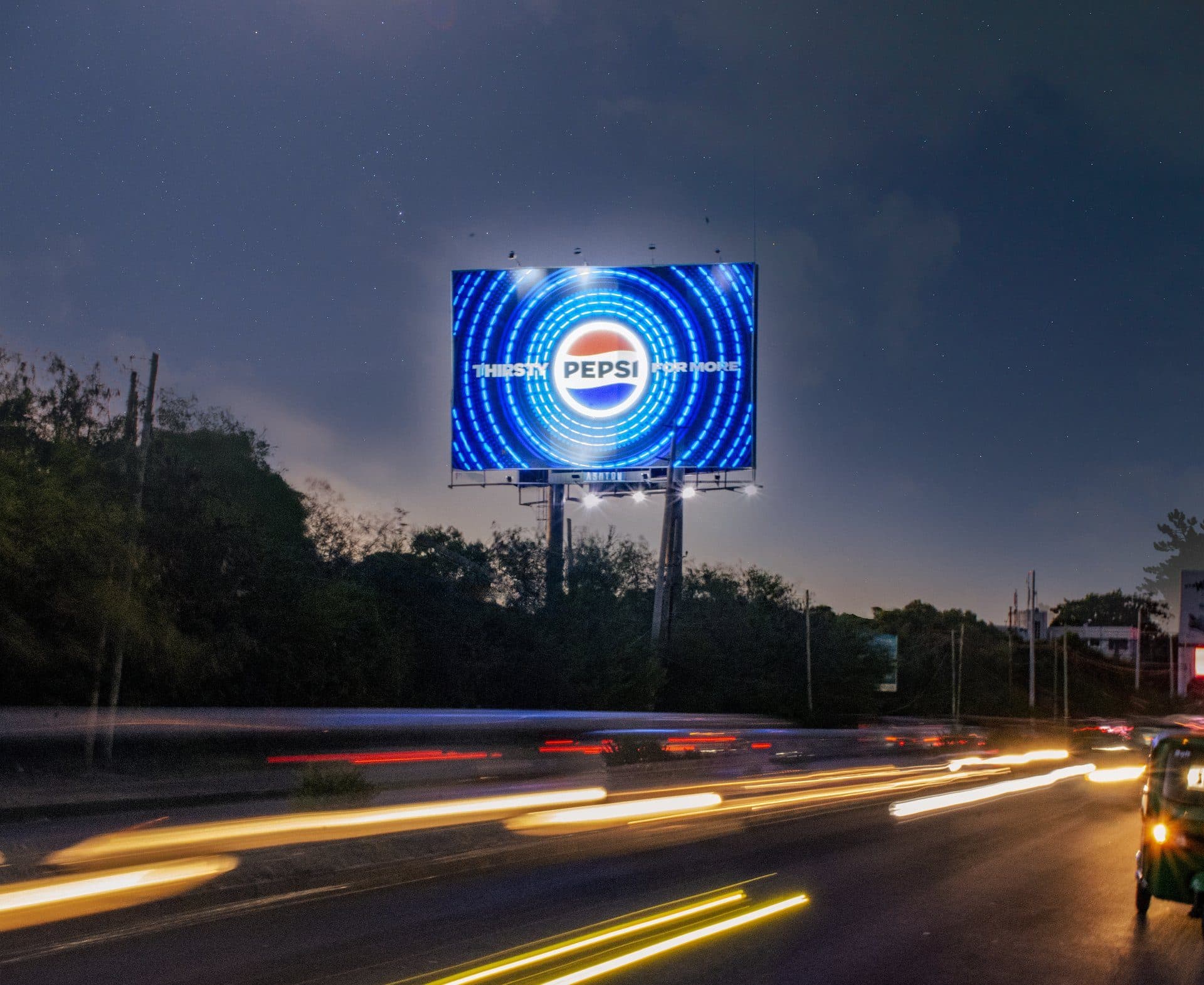 A Pepsi billboard lit up at dusk on a main road in Dar es Salaam